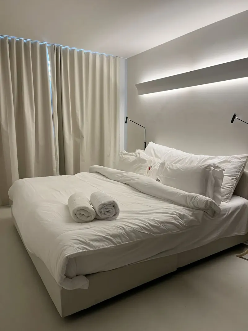 A freshly made bed with folded towels in a bright holiday rental